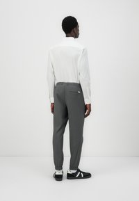 Gray tapered pants with an elastic waistband, back pocket detail, and cuffed ankles, paired with a white collared shirt and black sneakers.