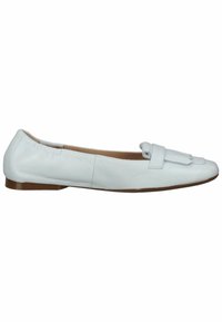 Mocassin plat en cuir blanc avec semelle basse marron et boucle décorative avec pompons sur le devant, vue de côté sur fond blanc.