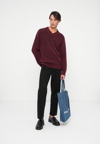 Burgundi lõngast v-kaelusega särk, mustad sirged püksid, mustad kingad ja sinine kangast kott valgete tähtedega. Puhtad, minimalistlikud jooned.