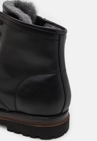 Gros plan sur une botte d'hiver en cuir noir avec doublure en polaire grise et semelle en caoutchouc robuste, marquée du logo "bugatti" sur le côté.