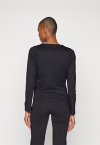 Svart langermet skjorte med rund hals, tettsittende design og glatt tekstur. Bakvinduet viser minimale sømmer og en ren finish.