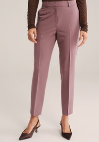 Spodnie lawendowe na miarę o prostym kroju, wykonane z gładkiej tkaniny, z przednimi kieszeniami, w zestawieniu z ciemnobrązowymi butami na obcasie.