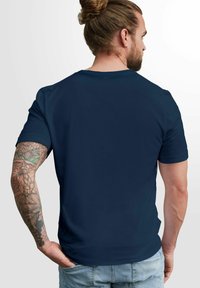Navy blue short-sleeved t-shirt with a standard crew neck. Smooth fabric texture, fitted design, and visible tattoo on the forearm.