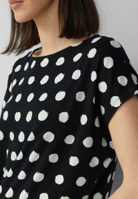 Zwarte top met korte mouwen met witte penseelstreep polka dots, zachte stof met een ontspannen pasvorm en een ronde halslijn.