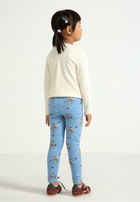 Ljus beige långärmad topp kombinerad med blå leggings med ett motiv av en hjort och blommor. Bruna skor med gröna och burgundy-accenter.