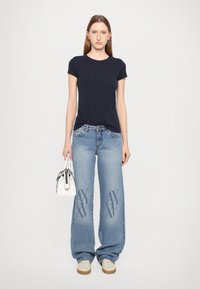 T-shirt aderente a maniche corte color navy, jeans larghi blu con leggeri sbiadimenti e dettagli del logo, abbinati a una piccola borsa bianca e sneakers.