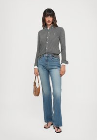 Chemise à rayures noires et blanches avec manches longues, associée à un jean évasé bleu clair et un petit sac à main marron.