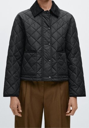 Veste matelassée noire avec boutons-pression et deux poches avant portée avec un pantalon marron, vue des épaules aux hanches.