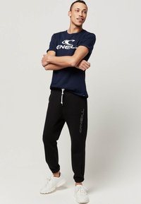 Navyblauwe katoenen T-shirt met wit logo, gecombineerd met zwarte joggingbroek met zijdelogo-detail. Afgerond met witte sneakers.