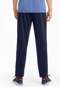 Navy athletic pants made of lightweight material, featuring a loose fit and elastic waistband. Worn with black sneakers with red accents.