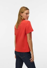 Rød bomuld T-shirt med korte ærmer, afslappet pasform og rund halsudskæring, båret med mørke denimjeans. Enkel og ren design.