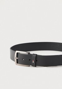 Czarny skórzany pasek z prostokątną srebrną klamrą i małą czarną pętlą z czerwono-białoniebieskim prostokątnym detalem logo.