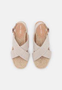 Vaaleat espadrillesandaalit ristikkäisillä kangasnauhoilla ja kootulla juuttipohjalla. Varustettu soljella ja sileällä nahkaisella sisäpohjalla.