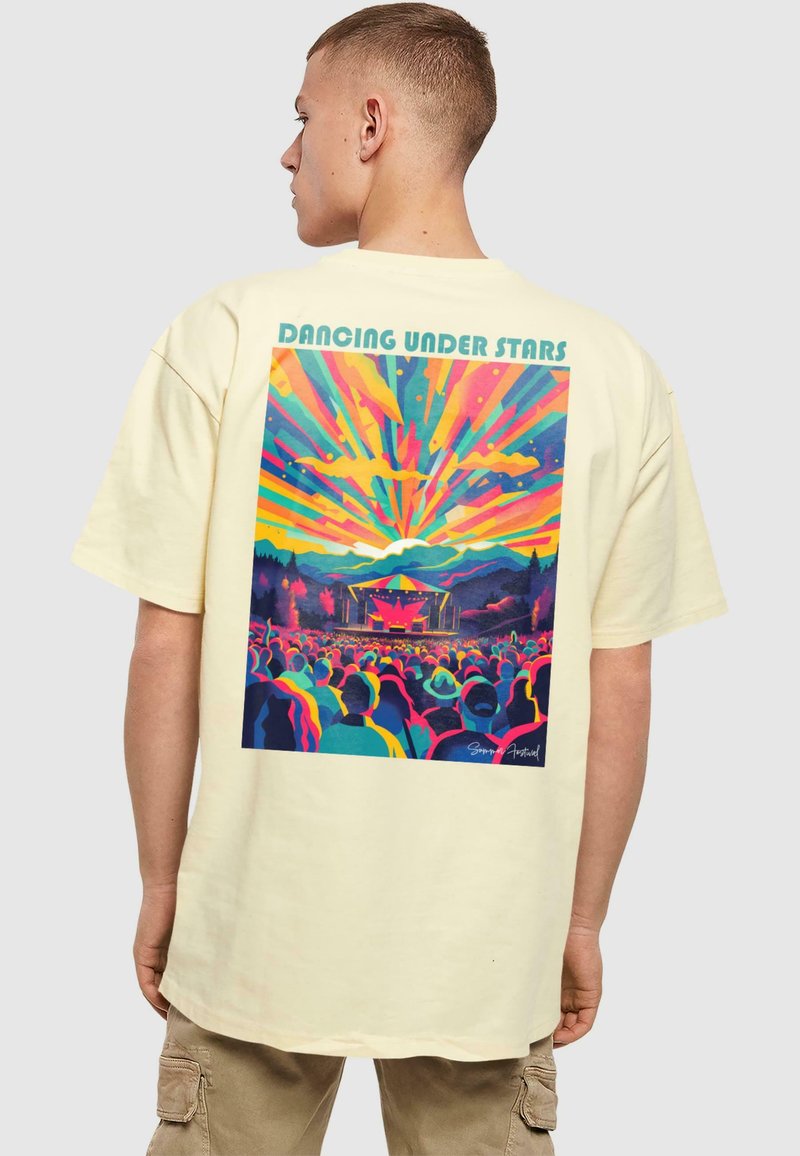 Camiseta de algodón color crema con un gráfico vibrante de una escena de concierto, con rayos coloridos y el texto "Bailando Bajo las Estrellas".