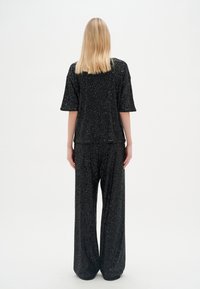 Completo di paillettes nere composto da un top morbido con maniche corte e pantaloni a gamba larga. Tessuto liscio con accenti luccicanti distribuiti ovunque.