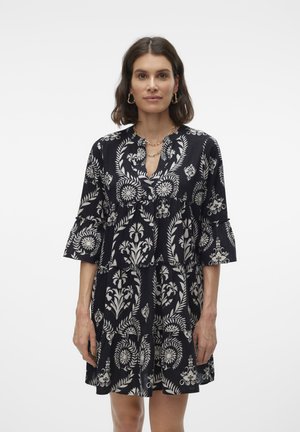 Robe noire avec motif floral blanc, design à étages et manches cloche trois-quarts. Encolure col avec un détail de bouton sur le devant.