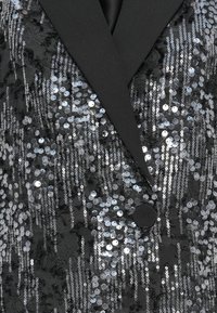Zwarte blazer versierd met zilveren pailletten, met een geknopt revers, knoopsluiting en een textuurstof met variabele plaatsing van de pailletten.
