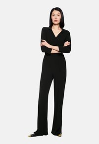 Black ribbed knit jumpsuit with long sleeves and a collared neckline, complemented by tapered pants and black shoes with gold accents.