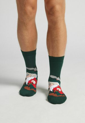 Groene sokken met een cartoon kerstman met een witte baard en een rood pak, geïllustreerd tegen een bruine achtergrond, knielang met een geribbelde bovenkant.