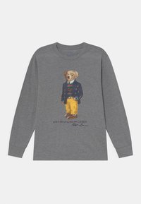 T-shirt grigio a maniche lunghe con una stampa fantasiosa di un orso vestito con un blazer blu, una camicia a righe, pantaloni gialli e scarpe marroni.