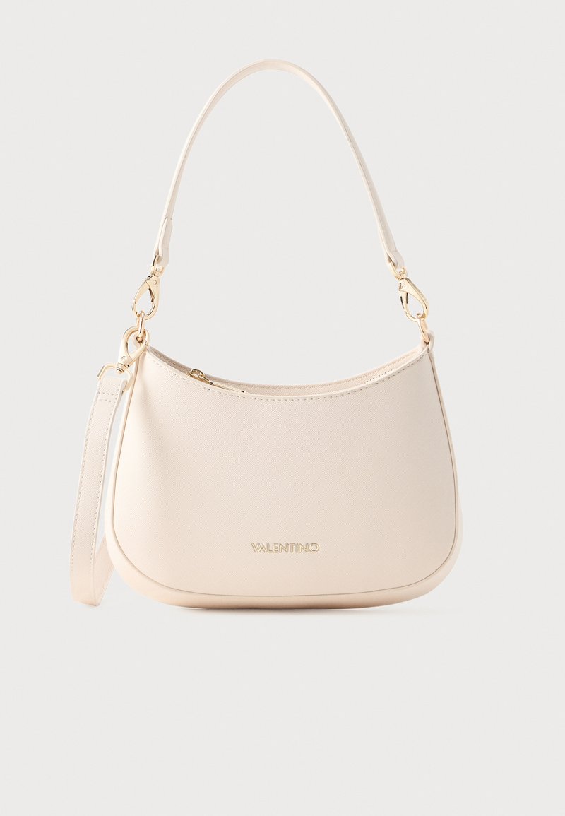 Svetlo béžová textúrovaná kabelka s oblým tvarom, zlatými doplnkami, odnímateľným ramenným popruhom a horným zipsom. Na prednej strane je logo.