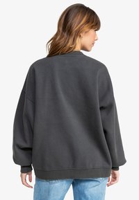 Felpa oversized grigia scura con scollatura rotonda, spalle ribassate e orlo a coste. Texture morbida e design casual.