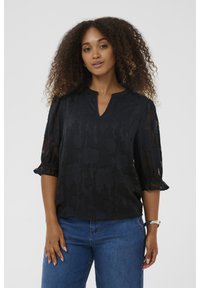 Melnas ziedu raksta blūze ar V veida kakla izgriezumu, 3/4 garuma pūkainām piedurknēm un volānu akcentiem, izgatavota no caurspīdīga viegla auduma. Apvienota ar ziliem džinsiem.