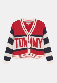 Czerwony i granatowy sweter z dzianiny z białymi paskami, z dekoltem w serek, zapięciem na guziki oraz dużym napisem "TOMMY" na klatce piersiowej.