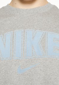 Gray cotton sweatshirt featuring a large, light blue "NIKE" logo across the chest and a small blue Nike swoosh underneath. Round neckline.