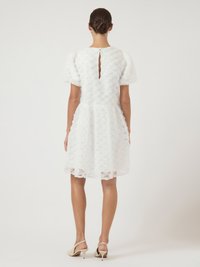 Λευκό φόρεμα με υφασμάτινη υφή λουλουδιών, φουσκωτά μανίκια και ανοιχτή πλάτη. Διαθέτει φουσκωτή φούστα και συνδυάζεται με μπεζ σλινγκμπακ τακούνια.