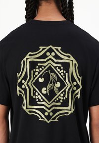 Sort bomulds T-shirt med et stort guld grafisk design på ryggen, med en diamantform, kirsebærmotiver og indviklede detaljer.