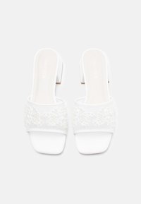 Sandales blanches à talon avec une bride texturée ornée de perles florales. Fini mat et lisse sur la semelle et design à talon bloc.