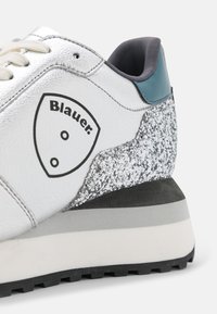 Baskets en cuir blanc avec un talon argenté scintillant, une semelle intermédiaire gris foncé et une semelle extérieure noire. Présentent un logo sur le côté.