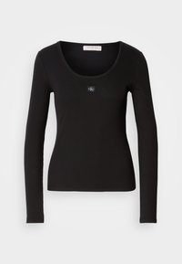Zwarte ribbel top met lange mouwen en een ronde halslijn, voorzien van een klein, vierkant Calvin Klein-logo-accent op de borst. Zachte textuur.