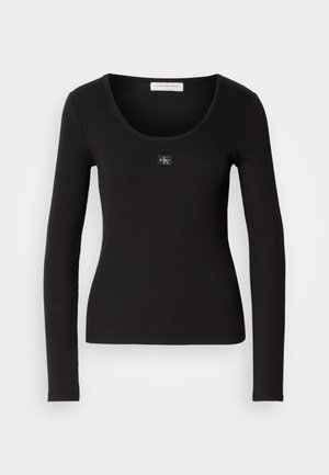 Melna garām piedurknēm ribota blūze ar ovālu kakla izgriezumu, ar nelielu kvadrātveida Calvin Klein logo akcentu uz krūšu daļas. Mīksta tekstūra.