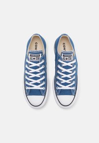 Blå kanvas sneakers med vita snören och gummisula. Har svarta detaljer och en etikett med texten "CONVERSE ALL STAR" på tungan.