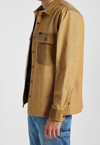 Bruine button-up jacket van textuurstof, met een borstzak, contrasterende kraag en lange mouwen, gecombineerd met blauwe jeans.