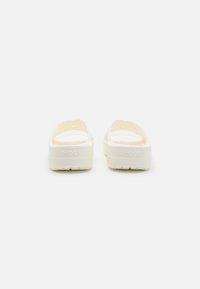 Sandales à glissière blanches Crocs avec un design lisse et arrondi, texture douce et bout ouvert. Comprend des trous de ventilation et une semelle texturée pour une meilleure adhérence.