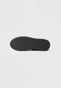 Semelle de chaussure noire avec un motif de grip texturé, affichée horizontalement sur un fond blanc uni.