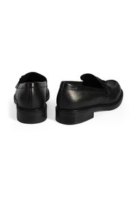 Zwarte leren schoenen met een gladde textuur, ronde neuspunt, lage hak en een decoratieve strik aan de voorkant. Subtiele stiksels.