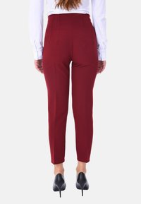 Pantaloni attillati borgogna con vita alta, gambe affusolate e una texture del tessuto liscia, abbinati a tacchi a spillo neri.