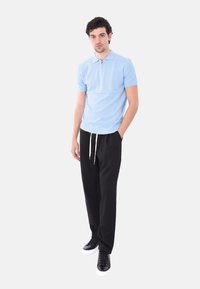 Polo azzurro chiaro a maniche corte con colletto a zip, abbinato a pantaloni neri a sigaretta e sneakers nere con suola bianca. Texture liscia.