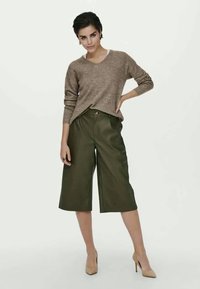 Brązowy sweter w prążki w połączeniu z oliwkowymi, wysokim talią kulotami. Kuloty mają zapięcie na guziki z przodu i luźny krój. Całość dopełniają beżowe obcasy.