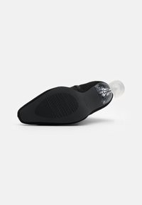 Zapato de ante negro con punta afilada y tacón transparente. Suela de goma texturizada. Diseño minimalista sin acentos adicionales.