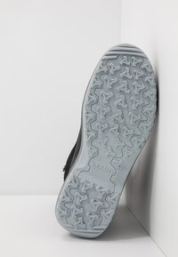 Schwarzer Schuh mit einer strukturierten grauen Gummisohle, die ein sternmusterförmiges Profil aufweist und mit "LOWA" gebrandet ist. An der Seite ist das Material aus Wildleder und hat ein niedriges Profil.