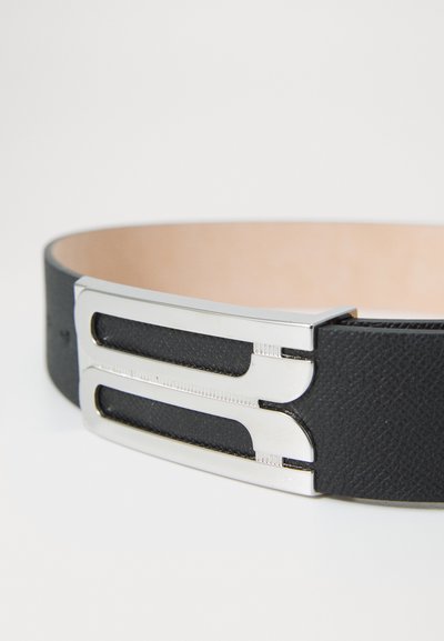 Black leather belt features a smooth finish with a silver metal buckle, designed with two cut-out sections and textured accents.