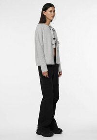 Grå stickad cardigan med knytning framtill, bärs över svarta cargobyxor. Har långa ärmar och en texturerad tyg.