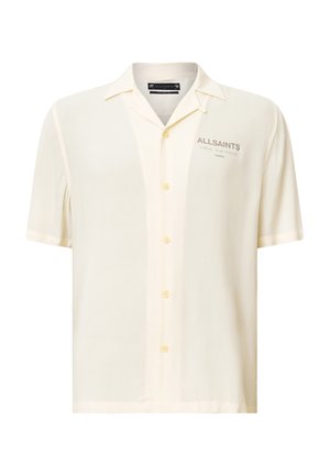 Chemise à manches courtes en tissu beige clair, avec un devant à boutons, coupe décontractée et un logo discret sur la poitrine.