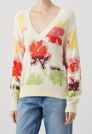 Pull en tricot avec un col en V profond, présentant un fond crème et des motifs de feuilles multicolores en rouge, jaune, vert et marron.