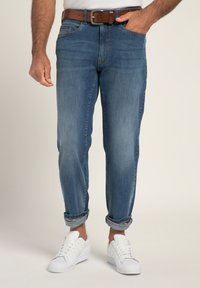 Jeans de denim azul claro con un corte relajado, puños enrollados y un cinturón de cuero marrón. Combinados con zapatillas blancas, exhibidos sobre un fondo neutro.